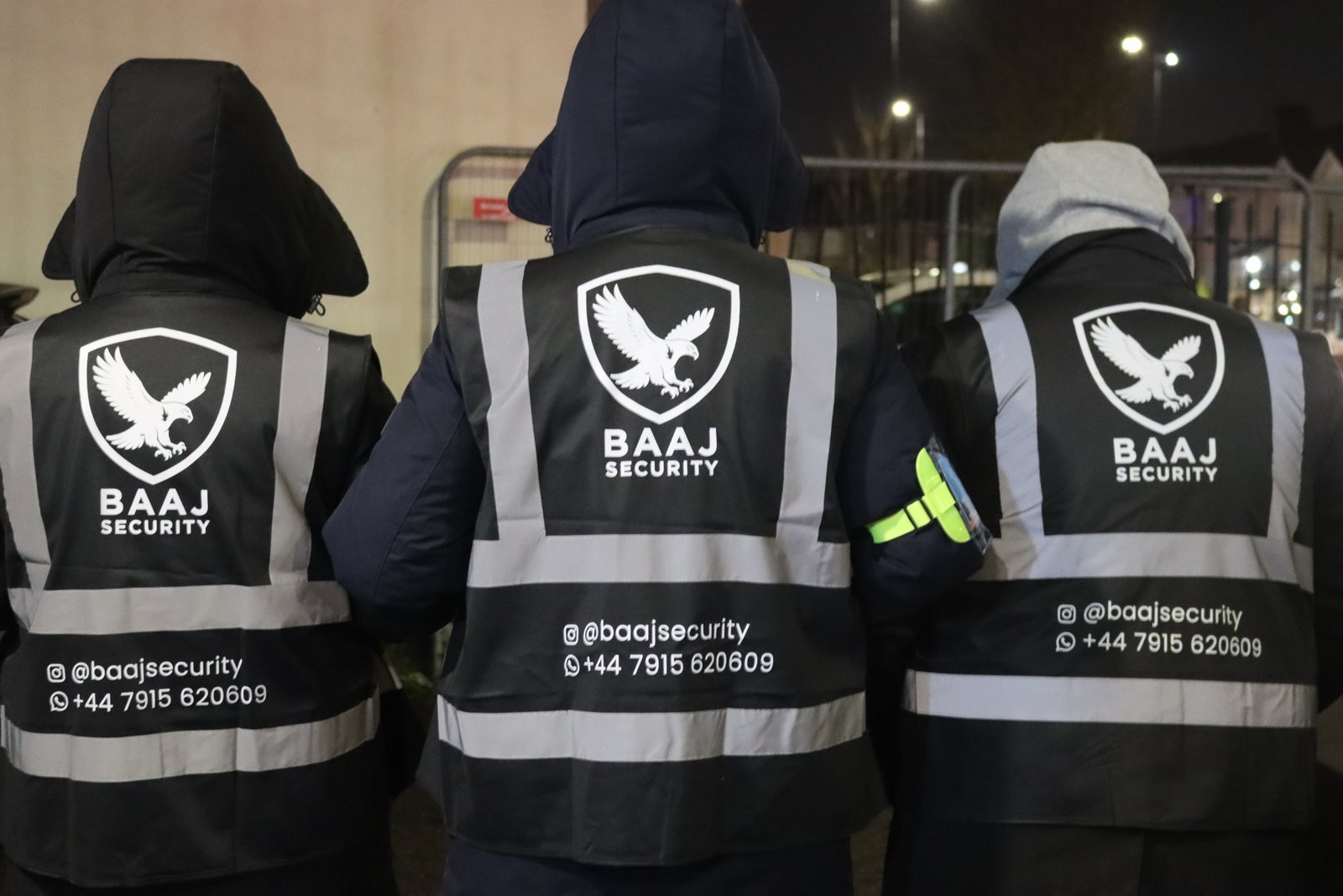 Three SIA-licensed Baaj Security operatives on duty at night in branded Baaj Security hi-vis, 2026